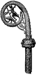 Illustration of the head of a bishop's staff, also called a crosier. The head is a serpent curled around another reptilian figure and a man with a staff. The serpent symbolizes that the bishop is responsible for the blood of his parish. The lower part is highly ornamented with vines, etc.