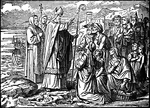 Illustration of Saint Patrick on the shores of Ireland, with bishop's miter and crosier, and other clergy behind him. He is holding his hand in blessing over several men, women, and children. Women kneel on the ground, one with a basket of fish. A little boy and girl watch the saint. A boat can be seen on the water and mountains rise in the background. Snakes slither on the ground in front of Saint Patrick.