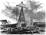An illustration of an iron derrick, a lifting device composed of one mast or pole which is hinged freely at the bottom. It is controlled by lines (usually four of them) powered by some means such as man-hauling or motors, so that the pole can move in all four directions. A line runs up it and over its top with a hook on the end, like with a crane. It is commonly used in docks and onboard ships. Some large derricks are mounted on dedicated vessels, and are often known as "floating derricks".