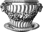 This flower pot with dish has a floral wreath designed wrapped around the center and a horned animal head on each side, right below the rim of the pot.