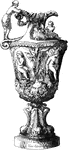 This vase is sculpted in marble. It has a design of cupid trying his bow in the center of the vase, and Venus holding cupid captive, bound with roses. The base is a pedestal with upright fish all around.