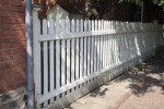 A White Picket Fence by a Brick Building