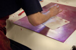 An artist paper-wiping an intaglio plate with red ink.