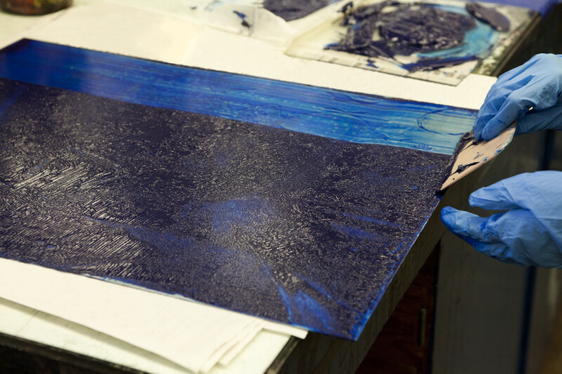 An artist pulling blue etching ink onto an etching plate.