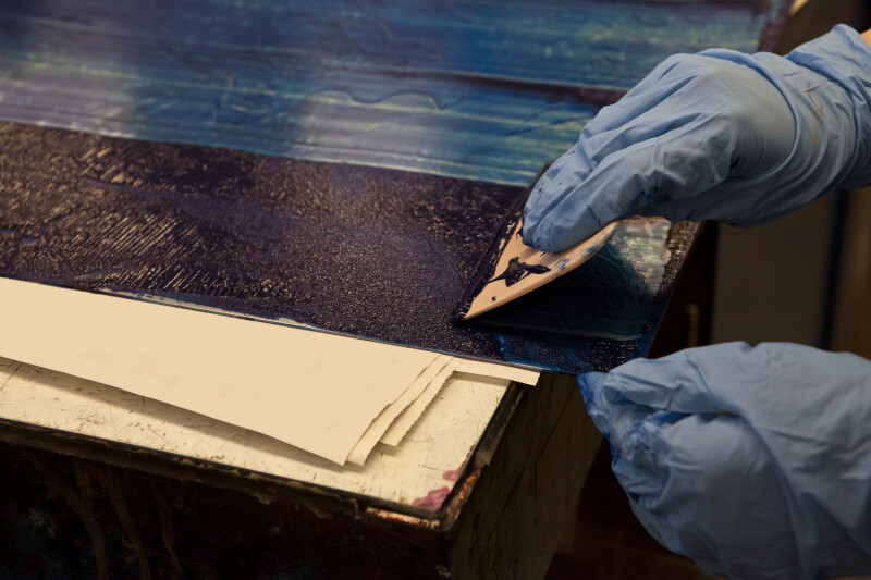 An artist scraping excess ink off of an etching plate.