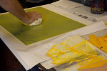 An artist wiping an etching plate with yellow ink.