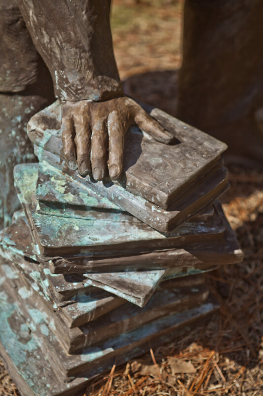 The Hand of a Bronze Sculpture Resting on a Stack of Books