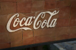 White Coca-Cola Lettering Against a Brown Wall
